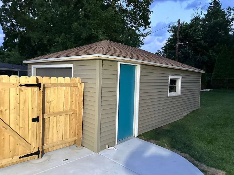 Completed garage with a new shingle roof, fresh siding, and cedar fence by Ultra Roof LLC in Greendale, WI